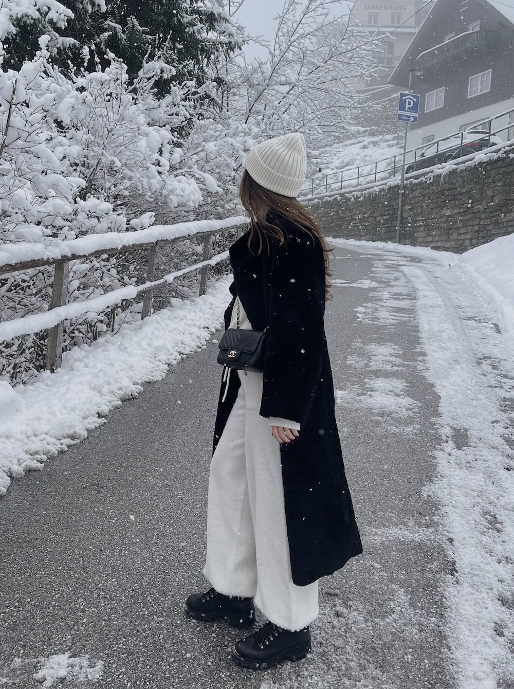 a woman wearing oversized grey sweatpants, a long black coat, a white beanie, and black winter boots