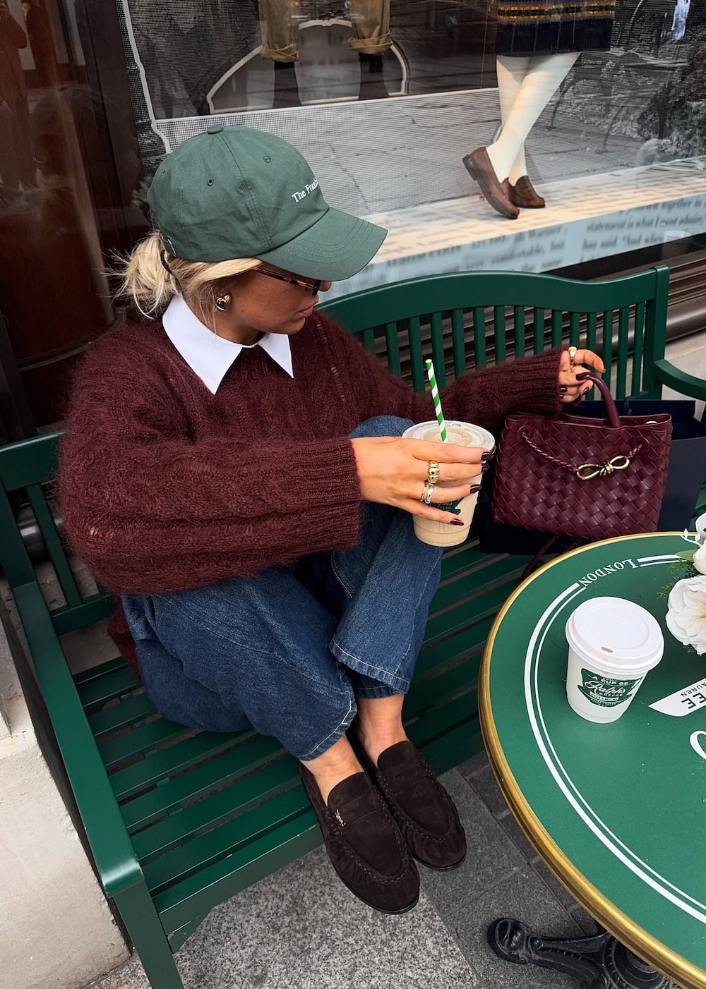a woman wearing blue jeans, suede loafers, a red sweater, and a green cap