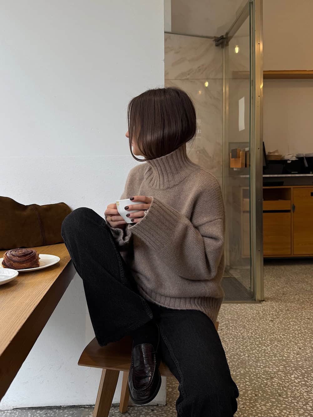 a woman wearing black jeans, black loafers, and a brown turtleneck