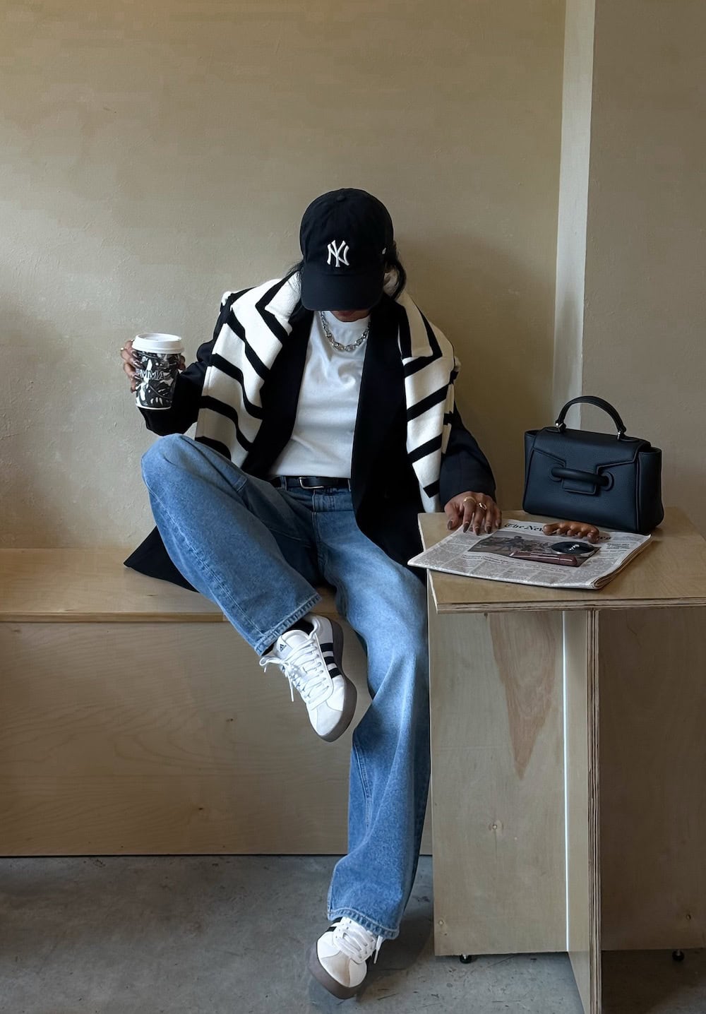 a woman wearing blue jeans, a white tee, an oversized blazer, white sneakers, and a striped sweater