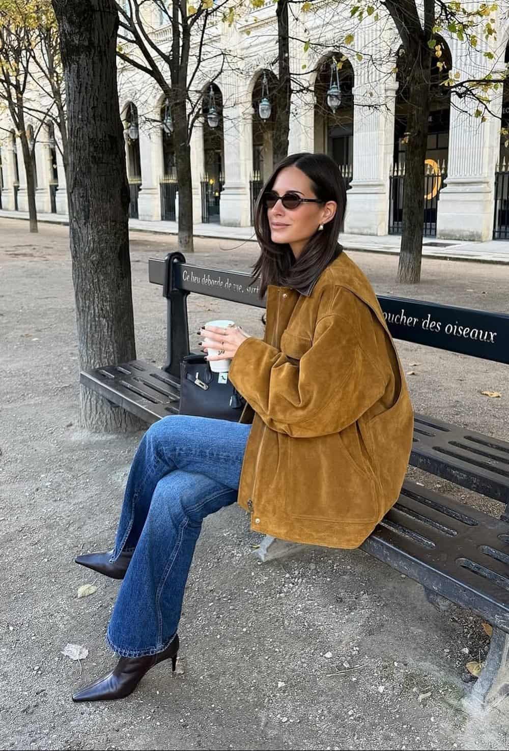 a woman wearing blue jeans, heeled boots, and a brown suede jacket