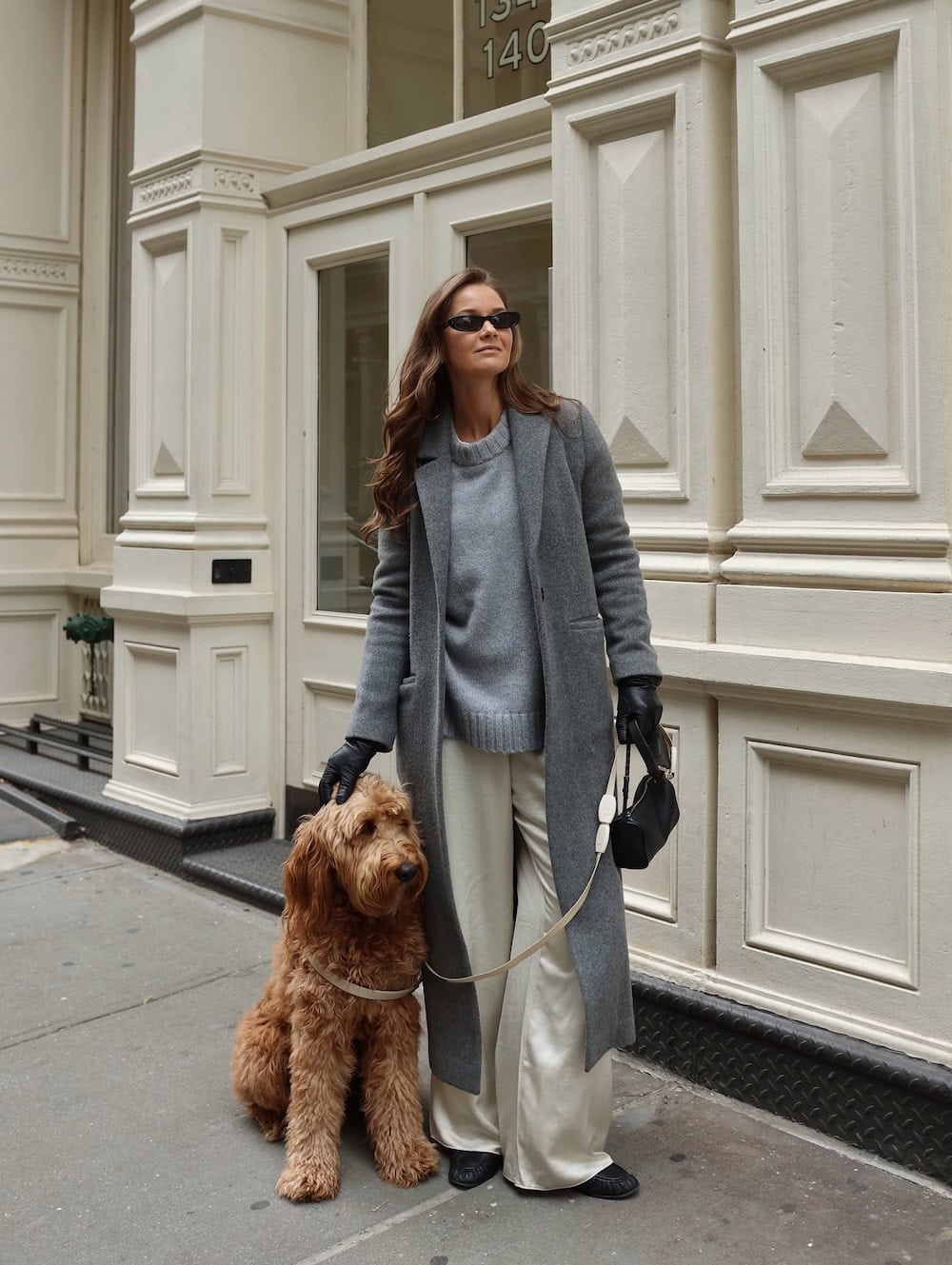 a woman wearing white slacks, a grey sweater, and a long grey coat