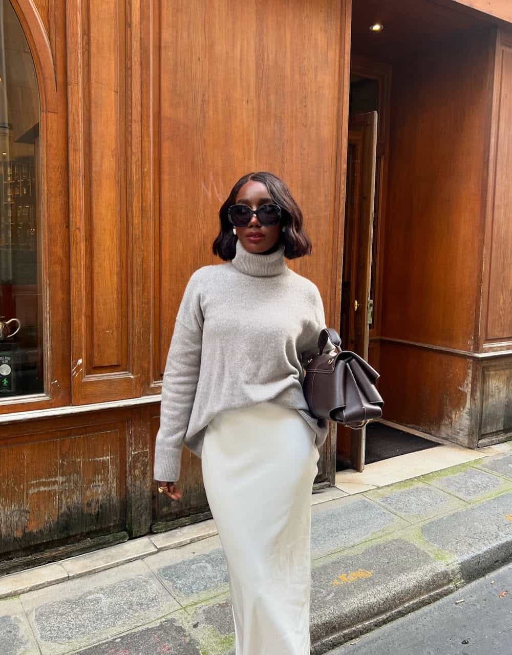 a woman wearing a white silk midi skirt and a light grey turtleneck sweater
