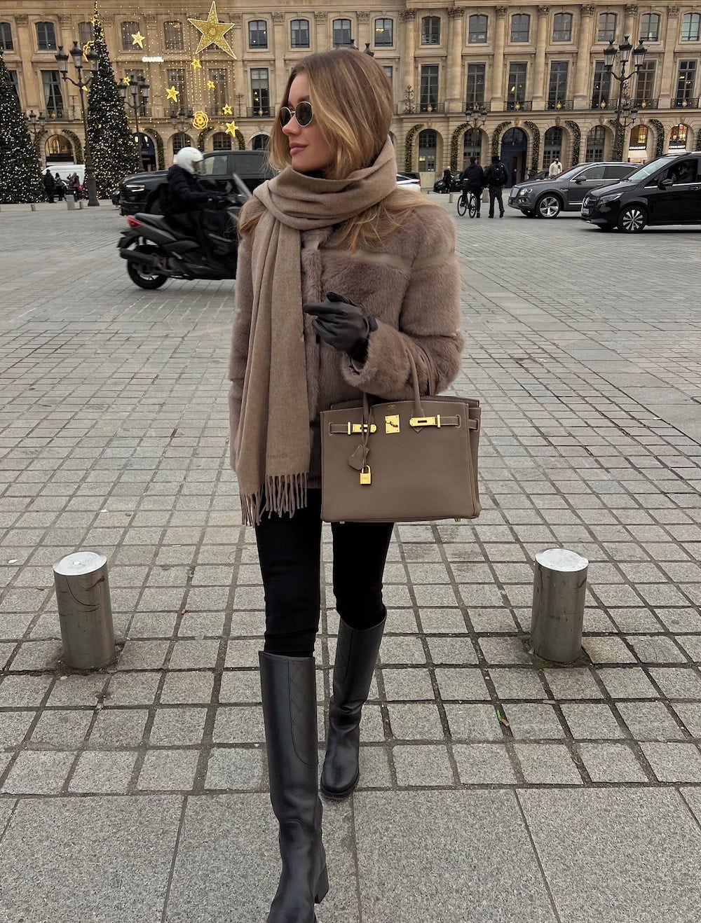 a woman wearing black leggings, tall black boots, a faux fur coat, and a long fringed scarf