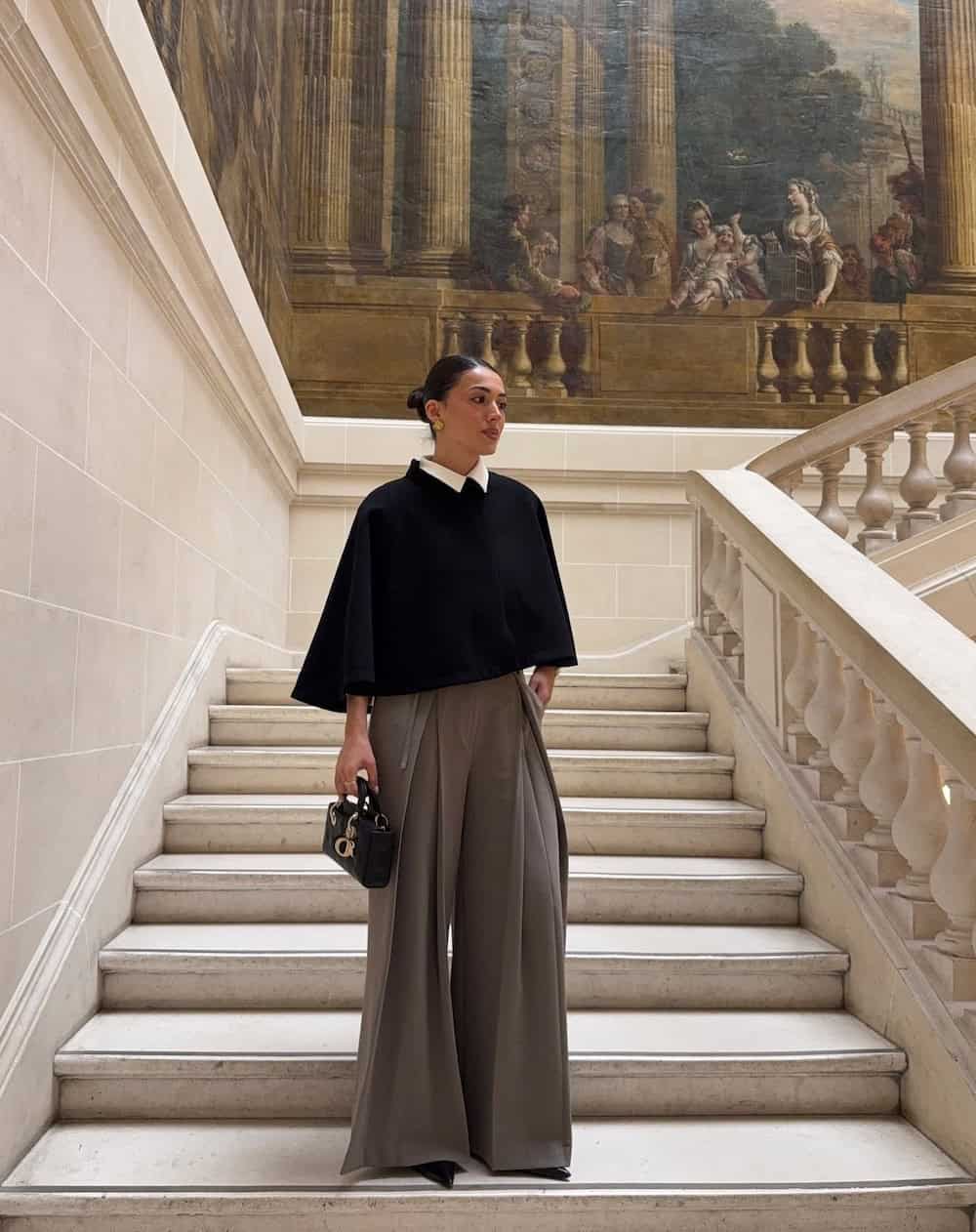 a woman wearing wide leg grey trousers and a black cropped cape top