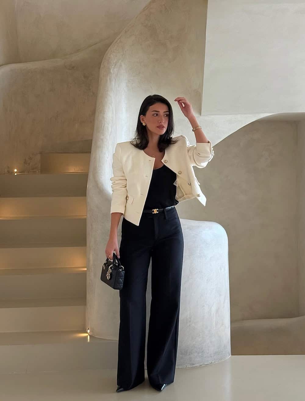 a woman wearing black trousers, a black scoop top, an ivory cardigan, and black pumps