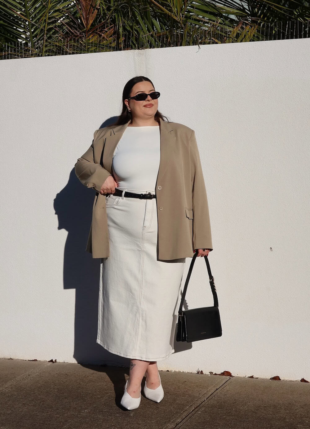 a woman wearing a white denim midi skirt, a white top, a beige blazer, and white heels
