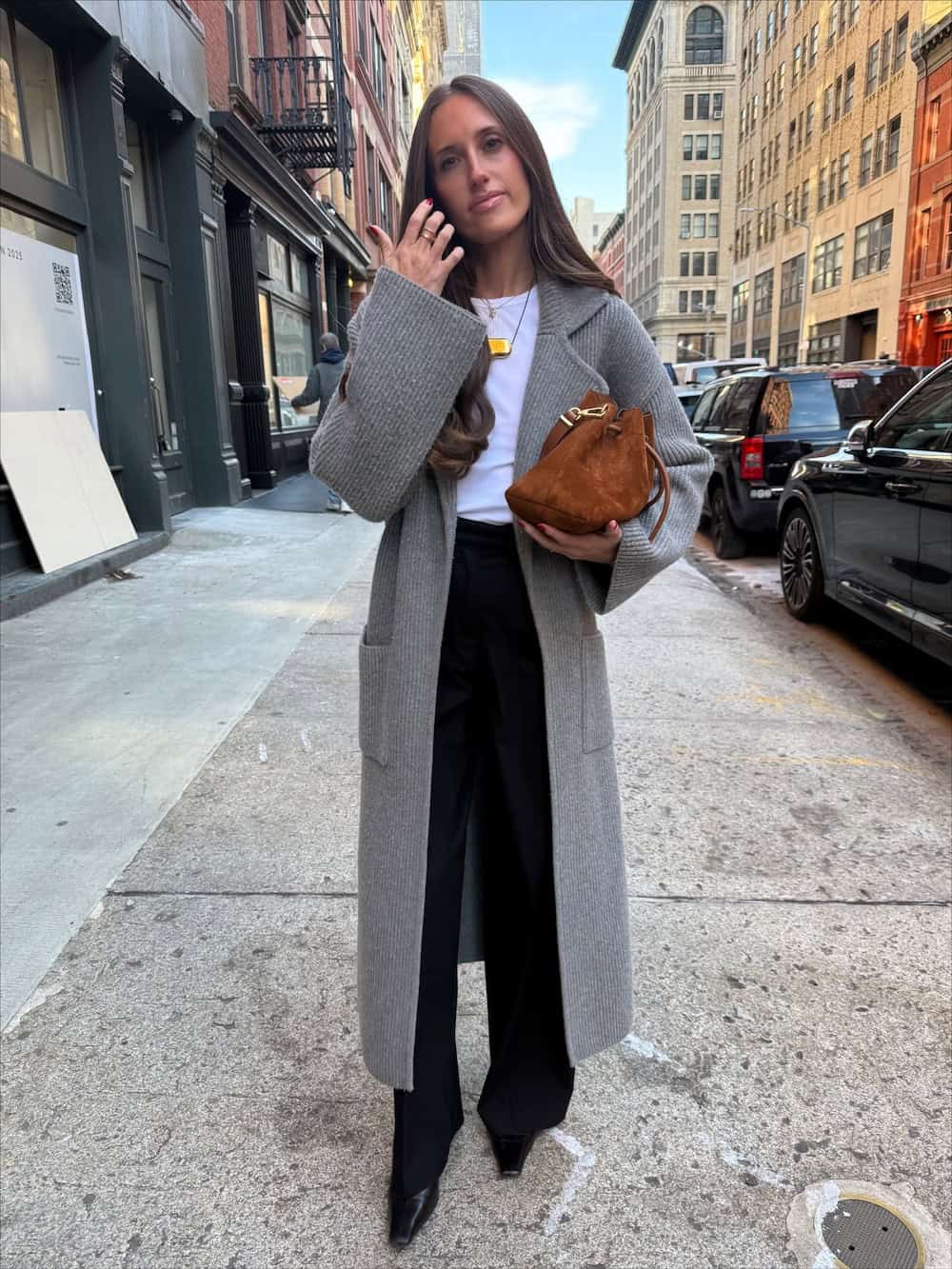 a woman wearing black slacks, a white tee, a long grey cardigan, and black heels