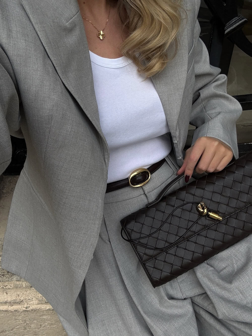 a woman wearing a grey suit set and white tank with black leather accessories