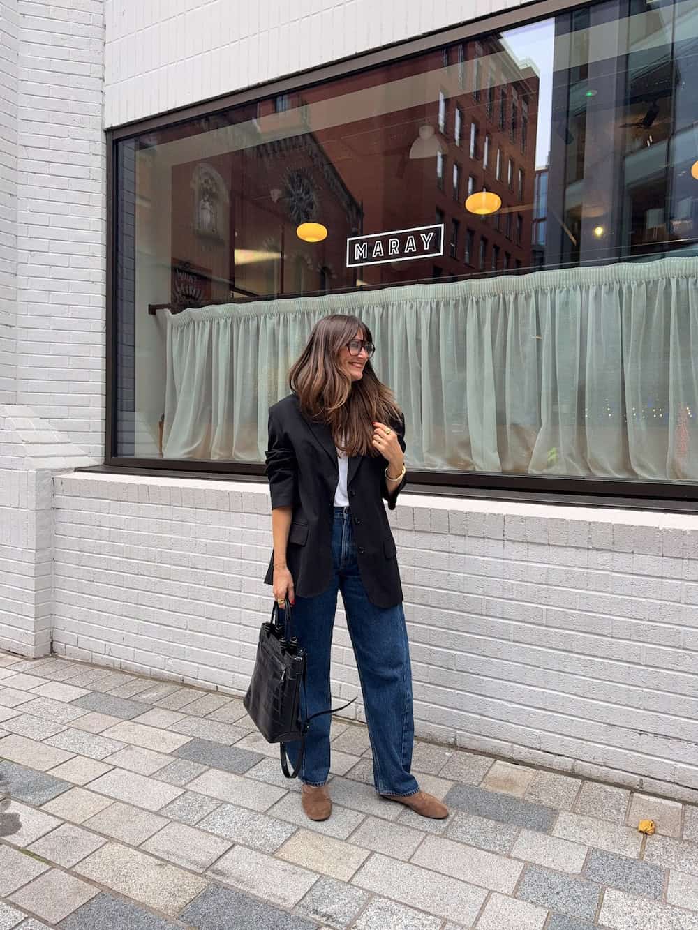 a woman wearing blue jeans, a white tee, a black blazer, and brown suede flats